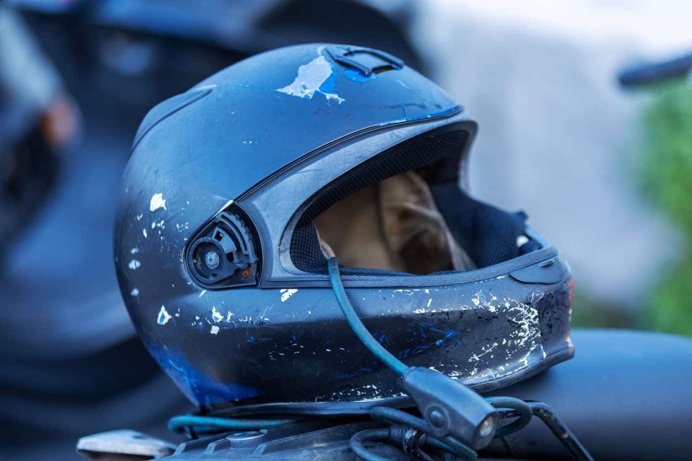 Close-up of a scuffed, chipped full-face motorcycle helmet resting on a motorcycle seat